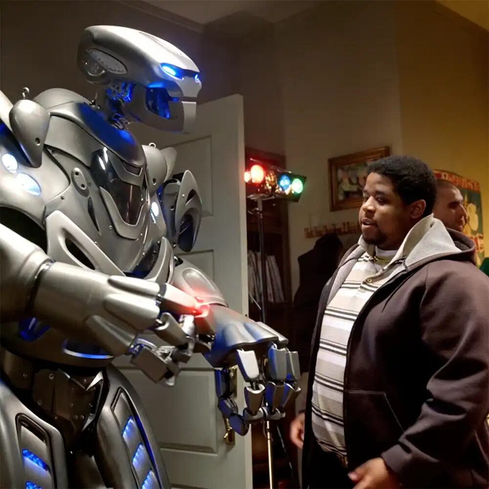 Titan the Robot stands in the entrance to a house party, talking to a man taking the keys from attendees.